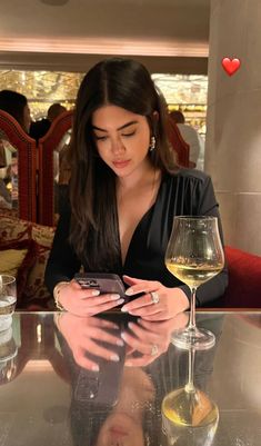 a woman sitting at a table looking at her cell phone next to a glass of wine