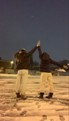 two people standing in the snow with their arms up and one person reaching for something