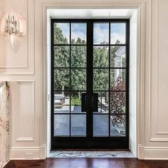 an open glass door in a white room with wood flooring and marble fireplace mantel