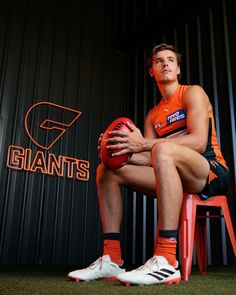 a man in an orange uniform sitting on a red chair holding a football and posing for the camera