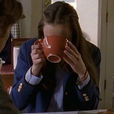 a woman holding a coffee cup in front of her face while sitting at a table