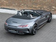 a silver sports car parked in front of a brick wall with the top down and its roof down