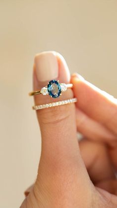 a woman's hand holding a ring with an oval blue stone and diamond band