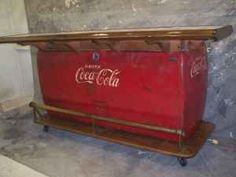 an old coca - cola cooler sitting on top of a wooden shelf next to a wall