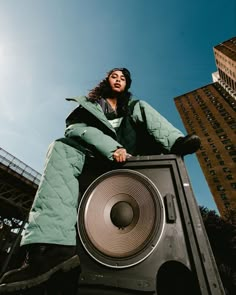 a woman sitting on top of a speaker near tall buildings