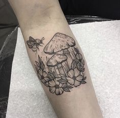 a mushroom and flowers tattoo on the left arm with a bee flying around it,