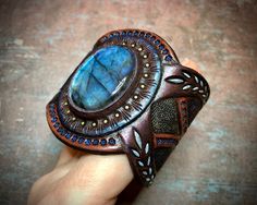 "\"Northern Bloom\" is a tooled leather bracelet with rare blue labradorite cabochon and metallic sheen. It would become a beautiful bright spot on your wrist. You can wear it with everyday clothes but it would also look great with romantic Boho style clothes. The braceletfits up to 6 /2\" (~16.5 cm) wrist. The bracelet on the pictures is a sample, for it was MADE TO ORDER. You may place a custom order and I will make a new bracelet for you in accordance with desired measurements and preferred c Romantic Boho Style, Boho Leather Jewelry, Rustic Cuff Bracelets, Leather Gifts For Her, Everyday Clothes, Romantic Boho, Labradorite Cabochon, Boho Leather, Hand Tooled Leather