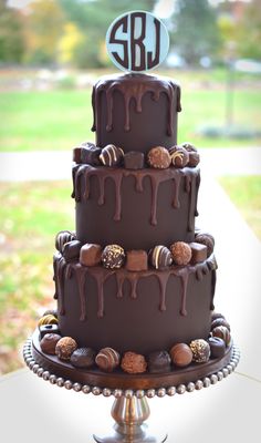 a three tier chocolate cake with the initials on top and covered in chocolate icing