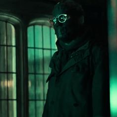 a man in a black trench coat and goggles standing next to a glass door