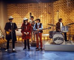 the bee gees on stage in front of a microphone, drums and drum set