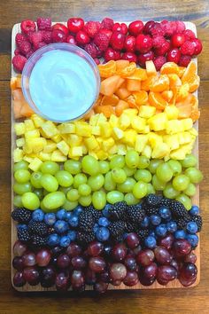 a wooden tray with grapes, raspberries, pineapples and other fruits