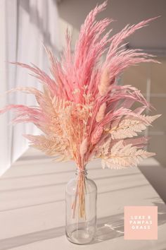 a vase filled with pink flowers sitting on top of a white table next to a window