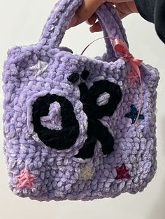 a hand holding a purple crocheted purse with black and white letters on it