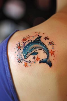 a dolphin tattoo on the back of a woman's left shoulder, with stars around it