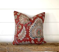 a red pillow sitting on top of a wooden bench next to a white brick wall