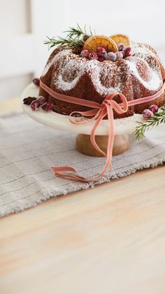 a bundt cake with icing and fresh fruit on top sits on a table