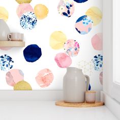 a white vase sitting on top of a counter next to a wall covered in colorful circles