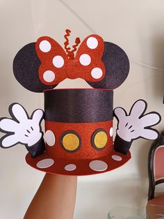 a hand holding up a paper hat with mickey mouse's ears and bows on it