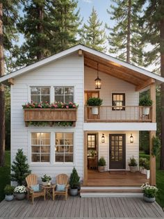 a small white house with wooden decking and potted plants on the front porch