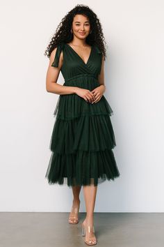 a woman standing in front of a white wall wearing a green dress with tiered layers