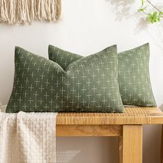 two green pillows sitting on top of a wooden bench next to a wall with a plant