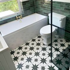 a white toilet sitting next to a bath tub in a bathroom with green tiles on the floor