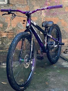 a purple and black bicycle parked next to a brick wall