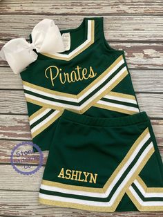 a green and gold cheer uniform with the word pirates on it, sitting on top of a wooden floor