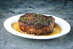 a piece of steak on a white plate with mustard and parsley sprinkled over it