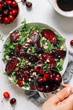 a bowl filled with cherries and greens next to bowls of cherries on a table