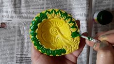 a person is painting a yellow and green plate