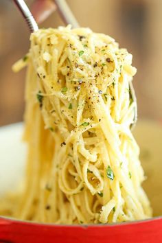 a red bowl filled with spaghetti and topped with parmesan cheese