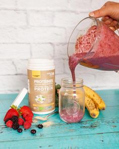 a person pouring some liquid into a jar with berries and bananas around it on a blue table