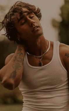 a young man with tattoos on his arm and chest, wearing a white tank top