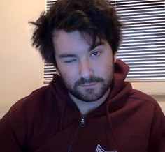 a man in a maroon hoodie is looking at the camera with his eyes closed