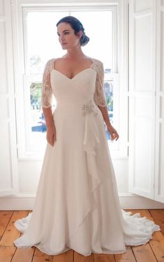 a woman standing in front of a window wearing a wedding dress