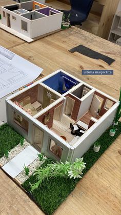 a model house sitting on top of a wooden table next to a pile of papers