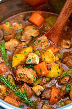 a pot full of stew with meat, potatoes and carrots on the side next to a wooden spoon