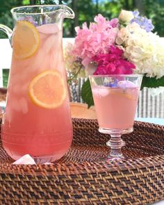 a pitcher and two glasses filled with pink lemonade on a wicker serving tray