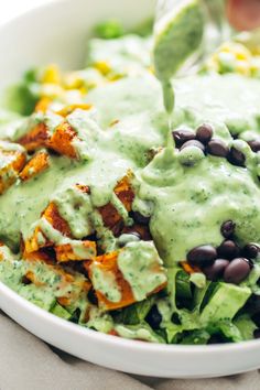 a bowl filled with salad and dressing being drizzled on top of it