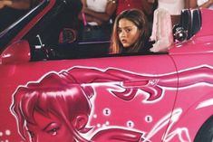 a woman sitting in the driver's seat of a pink car painted with an image of a horse