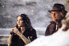 a man and woman standing in the snow with one holding her hand to her chest