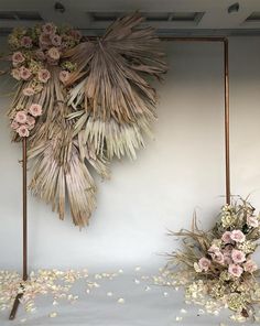 an arrangement of dried flowers is displayed on the wall next to a vase with pink and white flowers