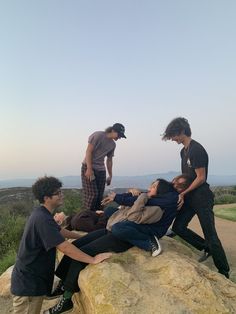 four people are sitting on top of a rock and one person is holding another man's leg