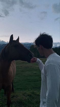 a man is petting the nose of a brown horse in a field with mountains in the background