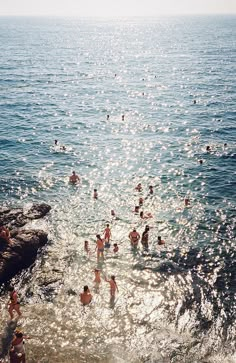 many people are swimming in the water at the edge of a cliff near the beach