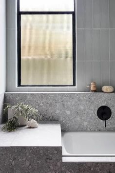 a white bath tub sitting under a window next to a sink with a plant on it