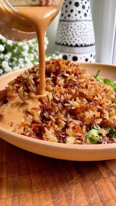 someone is pouring sauce on some food in a bowl with greens and flowers behind it