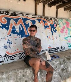 a man with tattoos sitting on a wall