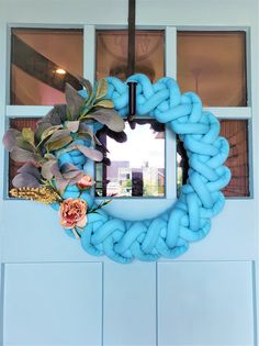 a wreath made out of blue yarn and flowers hangs on the wall in front of a window